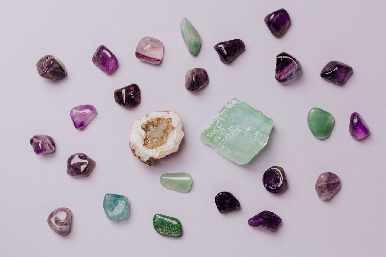 Services Flat lay of assorted polished gemstones including amethyst and jade on a light background.