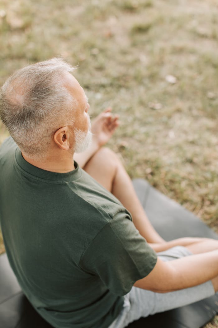 services-03 A senior man practices meditation in a serene park setting, focusing on breathing and wellness.
